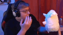 a man wearing headphones and glasses is holding a stuffed animal in his hand .