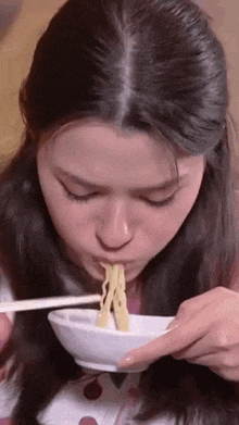 a close up of a woman eating noodles with chopsticks from a bowl .