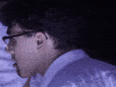 a close up of a man wearing glasses and a white shirt in a dark room