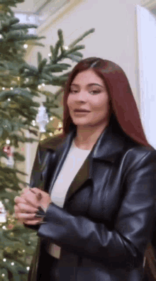 a woman wearing a black leather jacket is standing in front of a christmas tree .