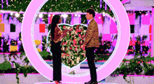 a man and a woman are standing next to each other in front of a heart shaped ring .