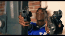 a man in a blue shirt is holding two guns in front of his face .