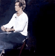 a man in a white shirt is sitting on a stage with his legs crossed .