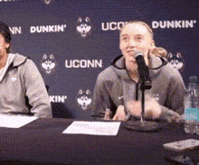 a woman is speaking into a microphone in front of a wall that says dunkin ' uconn