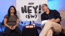two people are sitting in front of a sign that says hey