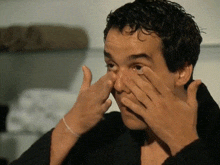 a man covering his face with his hands while wearing a black shirt