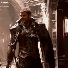 a man in armor with a necklace that says ' x ' on it stands in front of a building
