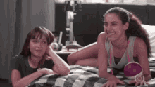 two girls are laying on a bed and one has a purple object in her hand