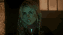 a woman with blonde hair and a scarf around her neck has a glowing key necklace around her neck