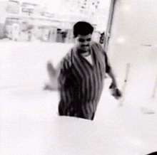 a black and white photo of a man in a striped shirt standing on a white surface .