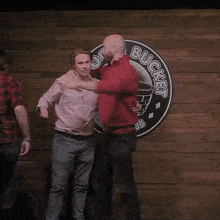 two men are hugging in front of a sign that says bucket on it