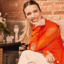 a woman wearing an orange shirt and white skirt is smiling