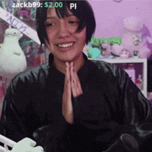 a woman in a black jacket is smiling and holding her hands together in prayer