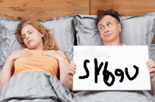 a man is holding a sign in front of a woman who is sleeping in bed