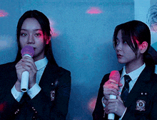 two girls in school uniforms are holding microphones and one has a badge on her jacket that says ' seoul ' on it