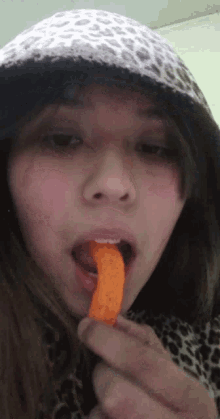 a girl in a leopard print hat is eating a cheetos chip