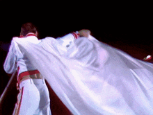 a man in a white cape is standing on a stage with his arms outstretched