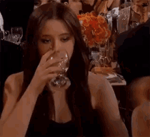 a woman with long hair is sitting at a table with a bunch of glasses and flowers in the background .