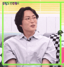 a man wearing glasses and a button up shirt is sitting on a couch and making a funny face .