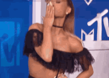 a woman in a black off the shoulder top is covering her face with her hand .