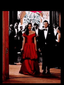 a woman in a red dress is walking next to a man in a tuxedo .