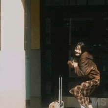 a woman squatting down with a suitcase in front of a building that says ms