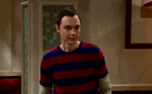 a man in a striped shirt is standing in a room with the word troglodytes written on the screen .