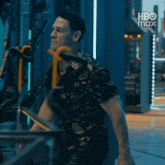 a man in a black and gold shirt is standing in front of a blue wall with hbo max written on it