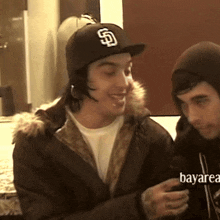 a man wearing a hat with the letter s on it is sitting next to another man