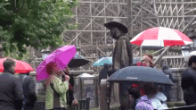a group of people holding umbrellas in front of a scarecrow statue