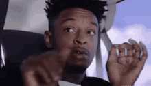 a young man is sitting in a car making a funny face and pointing at the camera .