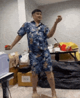 a man in a hawaiian shirt and shorts is standing in front of a cardboard box that says also
