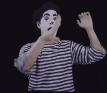 a man in a striped shirt and white face paint is making a mime face .