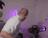 a man in a white shirt stands in front of a microphone with a purple light behind him