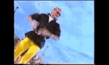 a man wearing yellow pants and a black shirt is dancing in front of a blue sky