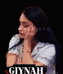 a woman with long hair is sitting down with her hand on her face and the word glynah is on the bottom .