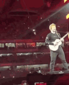 a man is playing a guitar on stage in front of a crowd .
