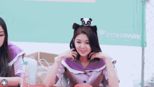 a girl wearing a cat ear headband is smiling in front of a sign that says " interpark "