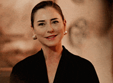 a woman wearing a black jacket and earrings is smiling