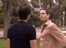 two men are standing next to each other in a park and having a conversation .