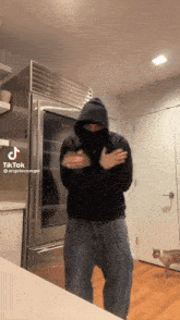 a man in a black hoodie is standing in front of a refrigerator with a cat behind him and a tiktok watermark