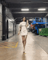 a woman in a white dress is walking down a hallway in a parking garage