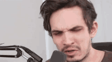 a man with a beard is sitting in front of a microphone making a funny face .