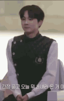 a young man in a black vest and white shirt is sitting on a chair .