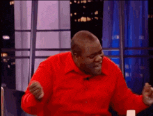 a man in a red shirt is making a funny face while sitting in front of a microphone .