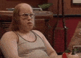 a bald man wearing glasses and a tank top is sitting at a table with a pumpkin .