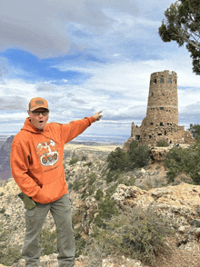 a man wearing an orange hoodie with a motorcycle on it points at something