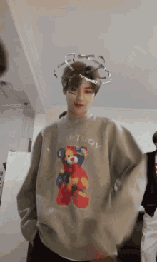 a young man wearing a sweater with a teddy bear on it is standing in a room