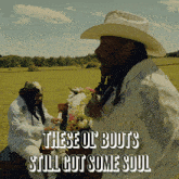a man in a cowboy hat is playing a piano in a field with the words " these ol boots still got some soul " below him