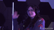 a woman wearing headphones stands in front of a microphone with gifrun.com written on the bottom